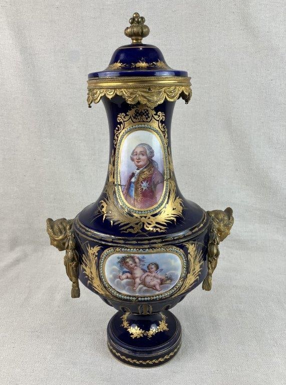 French Louis XVI Gilt and Cobalt Decorated Porcelain Covered Vase: Porcelain vase in the Louis XVI taste, richly decorated with gilt detailing and ormolu mounts in the form of Grecian busts, surmounted by a finial, with draped ornament around the upper rim. The body