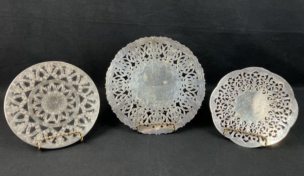 Silverplate Trivets: Group of three silver plate trivets with reticulated openwork designs, displaying classic decorative metalwork. The largest measures approximately 1/2â€³ H x 7 1/2â€³