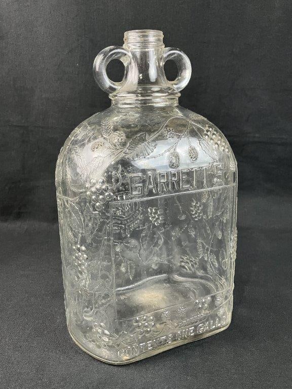 Early 20th Century Garrettâ€™s Wine Jar: Clear glass advertising jar with embossed grape and vine design, representative of early 20th century packaging and display ware. Measures approximately 12â€³ H x 5â€³