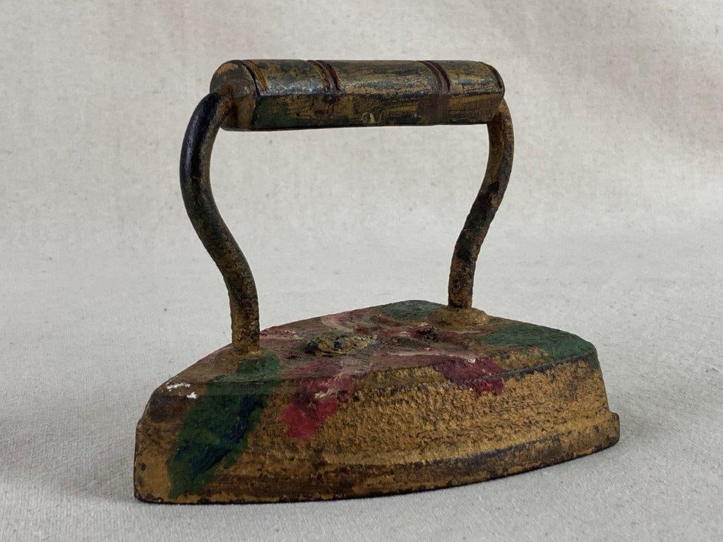 Folk Art Painted Sad Iron: A whimsical example of domestic folk art, this antique-style cast iron sad iron features a decorative brass-painted finish. The body of the iron is embellished with a hand-painted pink flower and