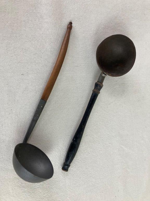 20th Century Metal Ladles: A pair of mid-century metal ladles featuring traditional turned wood handles. The first is a primitive-style ladle constructed with a tin bowl and a simple black-stained handle. The second is a fine