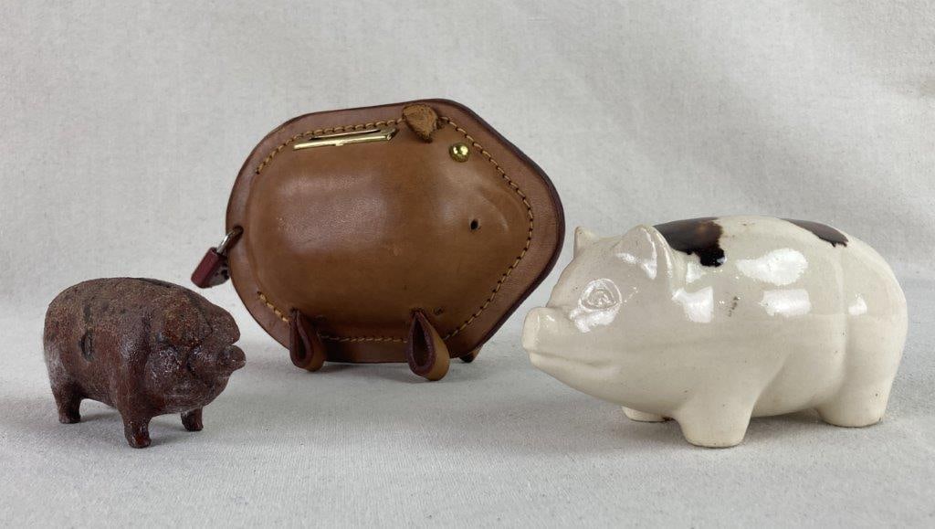 Three Pig Themed Still Banks: A whimsical trio of pig-themed still banks, each showcasing a distinct material and artisanal approach. The collection features a porcelain pig with a cream and spotted brown glaze, a smaller cast