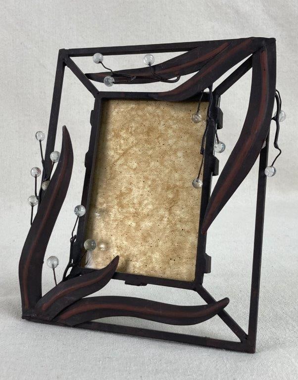 Metal Leaf Frame: This rectangular dark metal picture frame is an elegant marriage of organic forms and industrial materials. It is intricately adorned with metal leaf details, twig-like textures, and curious clear sph