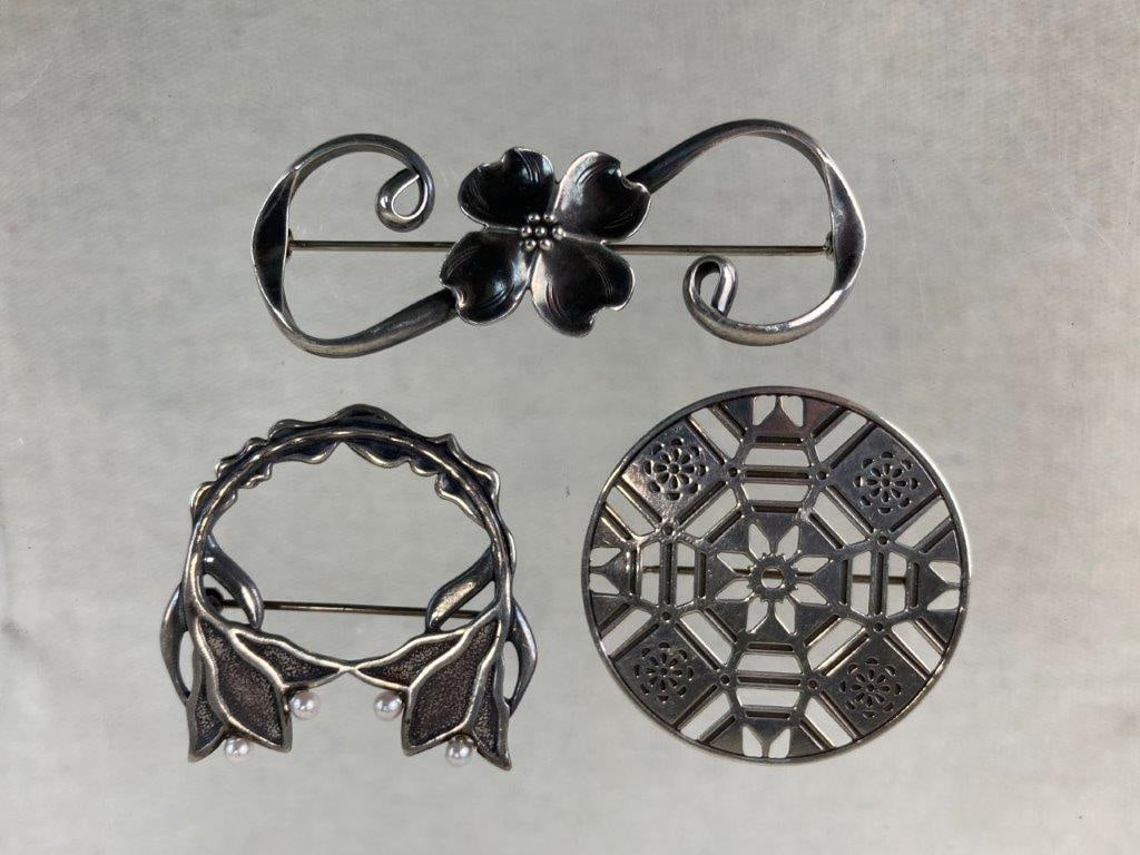 Three Sterling Silver Brooches Including Stuart Nye: This collection of three sterling silver brooches features a variety of beautiful floral designs, highlighted by a signature dogwood flower brooch by Stuart Nye of Asheville, North Carolina. The lot