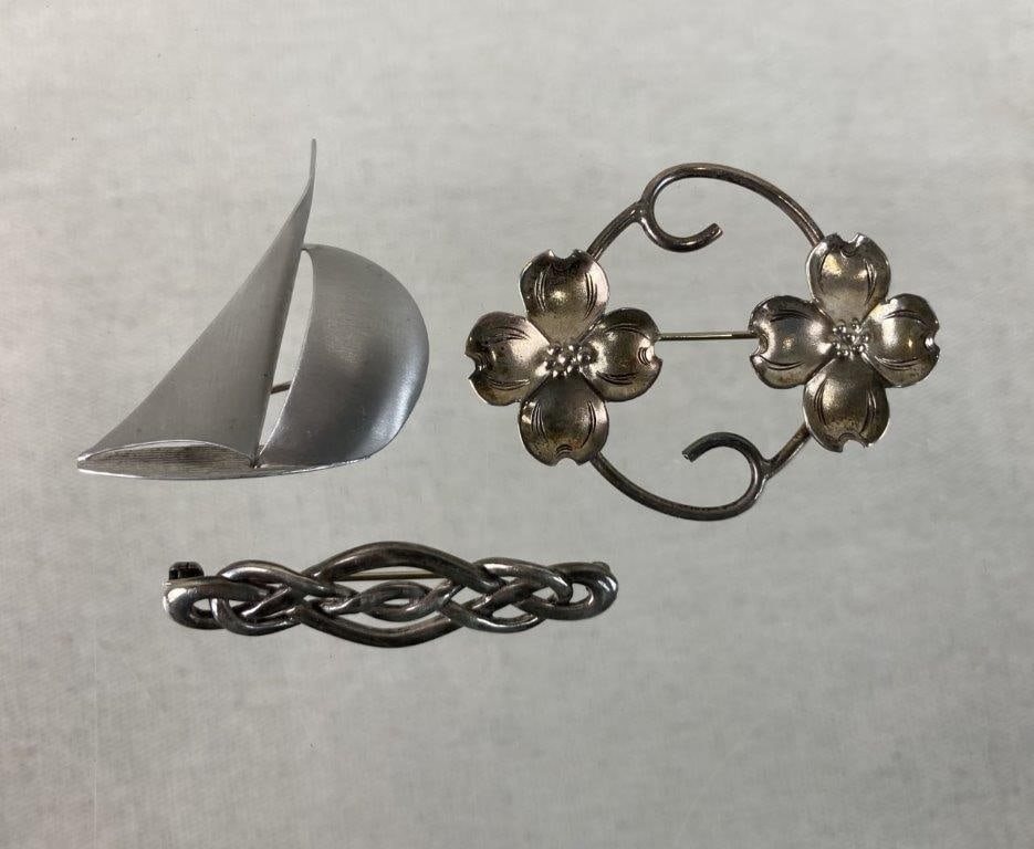 Three Sterling Silver Brooches Including Beau: This three-piece collection of vintage sterling silver brooches features a charming mix of nautical, floral, and traditional motifs. The assortment includes a simple sterling silver sailboat crafted