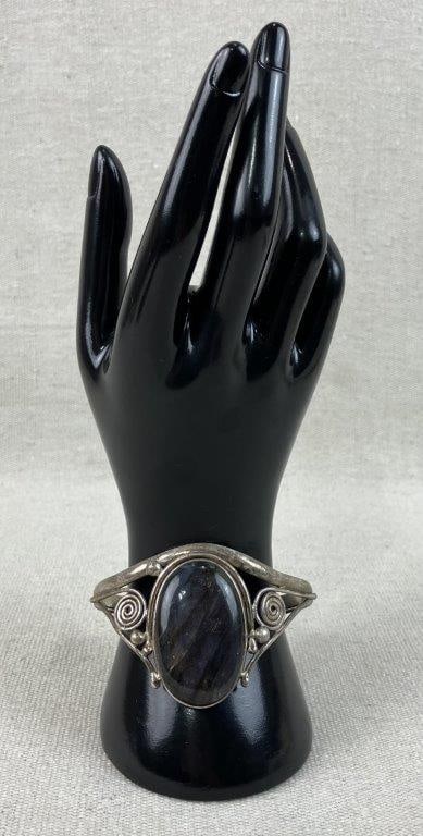 Sterling Silver Labradorite Cuff Bracelet: This handmade cuff bracelet showcases openwork metal shoulders adorned with stylized wire spire scrollwork and accent spheres that flank a large oval-shaped central labradorite stone. The piece is