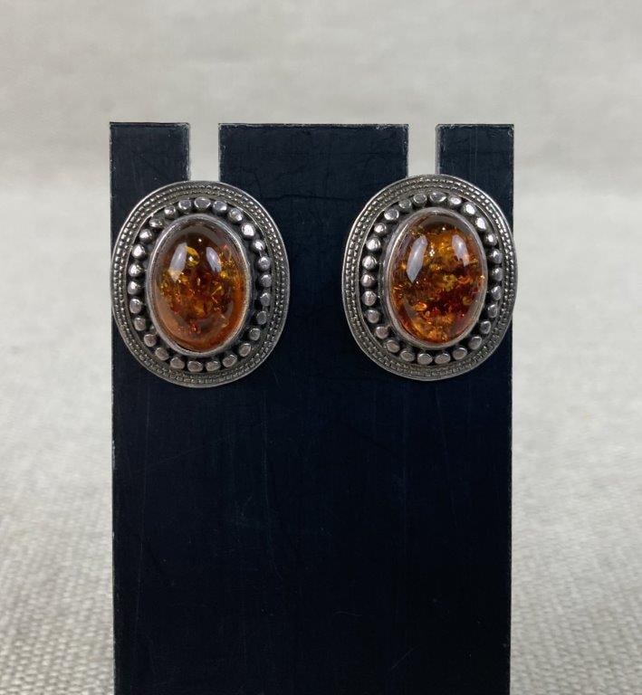 Sterling Silver and Amber Stud Earrings: These sterling silver stud earrings each feature a central amber cabochon set within an oval frame and accented by a decorative beaded silver border, with both pieces marked for silver content. An ind