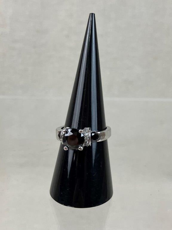 Silvertone Black Onyx Style Ring: Silvertone ring set with a central brilliant cut black stone, likely black onyx, within a raised gallery, flanked by bands of clear faceted stones to either side and accented by an additional smaller