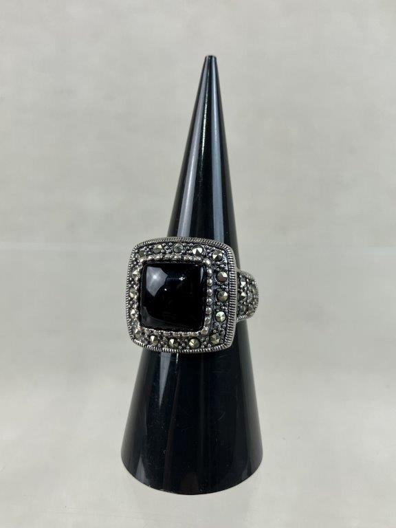Sterling Silver Black Onyx Ring: This sterling silver statement ring centers on a striking, cushion-cut black onyx stone framed by a glittering, pave-set border of marcasite stones that extends down the shoulders of the band. The rin
