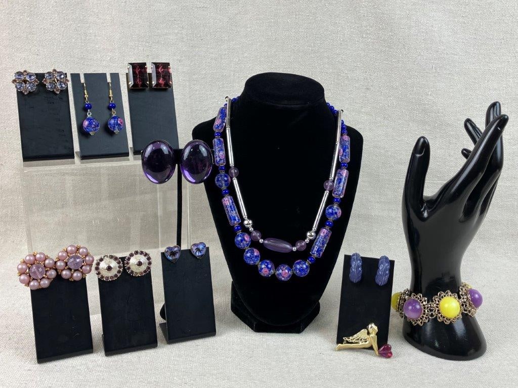Purple Themed Costume Jewelry Assortment Including Sarah Coventry: Group of twelve pieces of vintage costume jewelry in purple tones, including two necklaces, one a translucent acrylic floral style necklace with matching earrings, a cupid motif brooch set with a