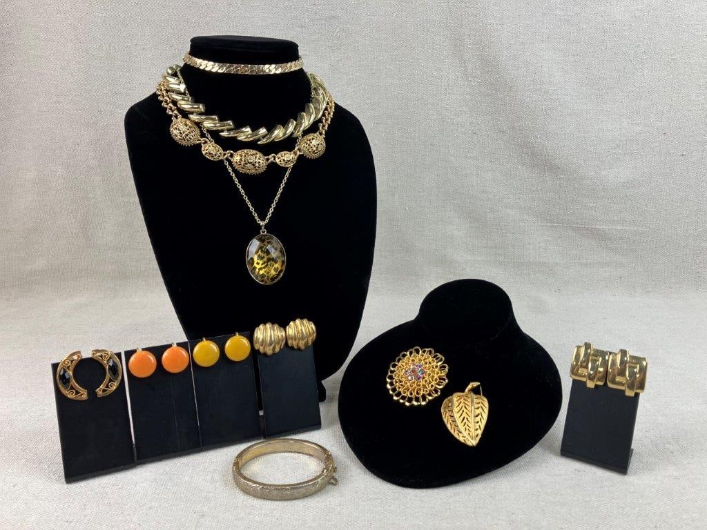 Gold Tone Vintage Costume Jewelry Assortment: Group of twelve pieces of vintage costume jewelry in gold tone, including two brooches, one a standout filigree form with a central iridescent rhinestone, two pairs of warm-toned lucite earrings, four