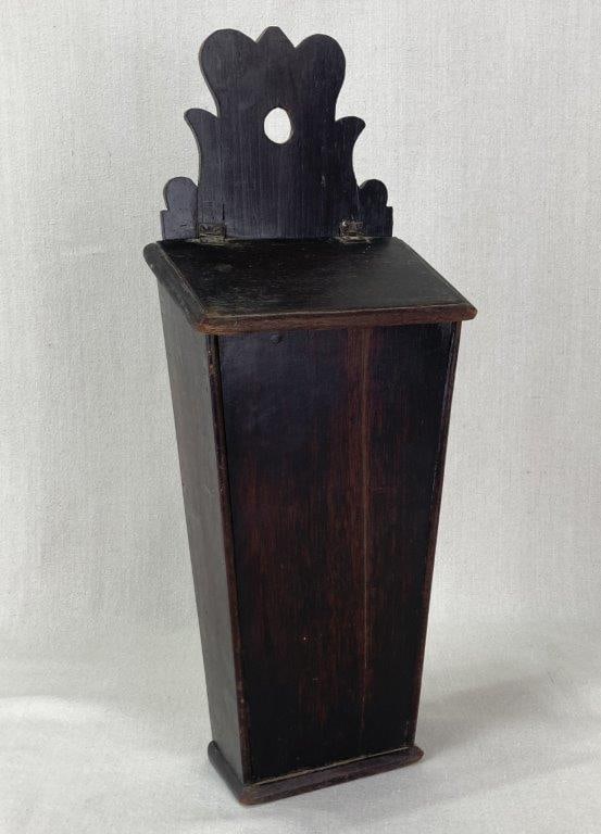 19th Century Simulated Mahogany Knife Box: A 19th century wall-mounted knife box with a simulated mahogany wood finish. The box tapers from the top down into a rectangular base and features a sloping hinged lid. It displays a high-backed