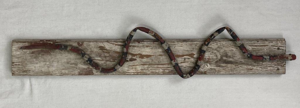 Polychrome Folk Art Snake: This folk art piece features a polychrome pipe snake mounted to a wood slab. Painted with a black, red, and white coloration, the sculpture displays a worn, aged patina. Measuring approximately 33