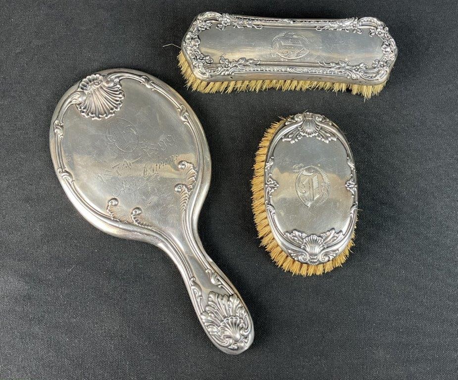 19th Century Sterling Silver Vanity Set: This elegant three-piece 19th-century sterling silver vanity assortment features two brushes and a hand mirror, each beautifully adorned with intricate repoussÃ© work in classic Rococo desig