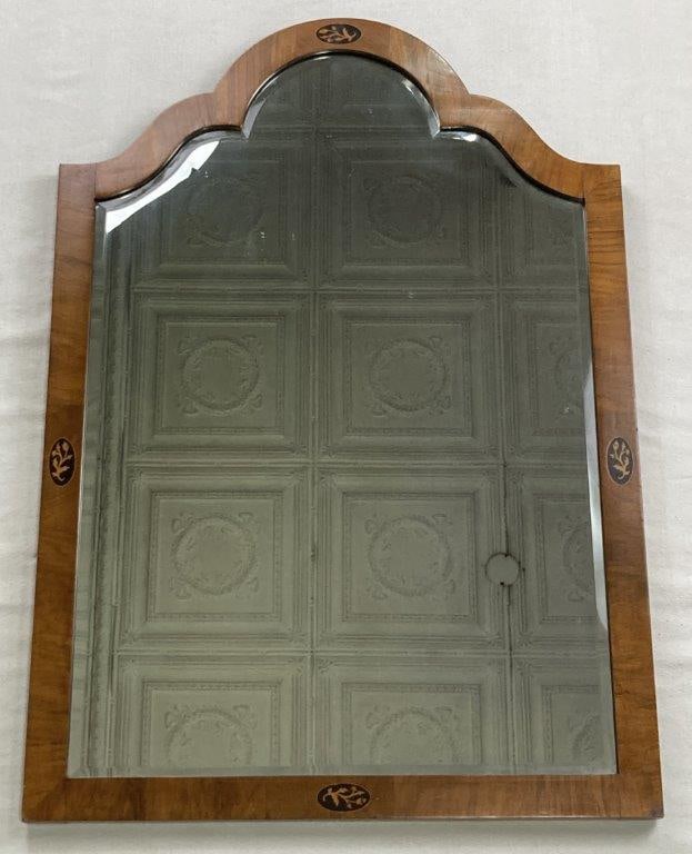 20th Century Inlaid Arched Mirror: A 20th century inlaid arched mirror featuring finely figured mahogany with an inlaid leaf motif. The piece is surmounted by an arched serpentine top and houses a beveled mirror plate. It measures