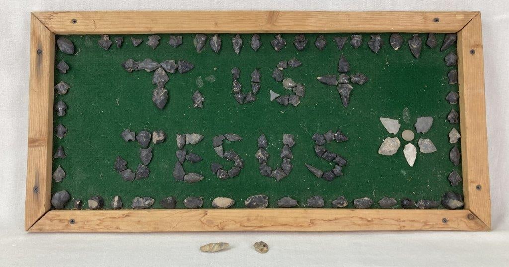 Folk Art Arrowhead Religious Motto: A folk art piece with a religious motto that says "Trust Jesus" and is made up of arrowheads, mounted to a wood board with a green fabric background. Measures approximately 14 1/2 in. H x 30 in. W x