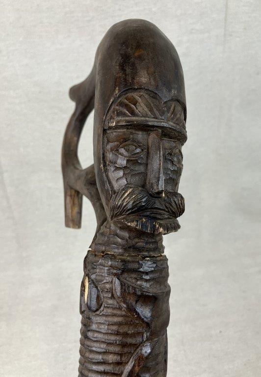 Folk Art Figural Cane: A charming piece of American folk art, this figural cane features a carved soldier's face on the front of the handle with a twisted grapevine motif winding down the shaft. It measures approximately