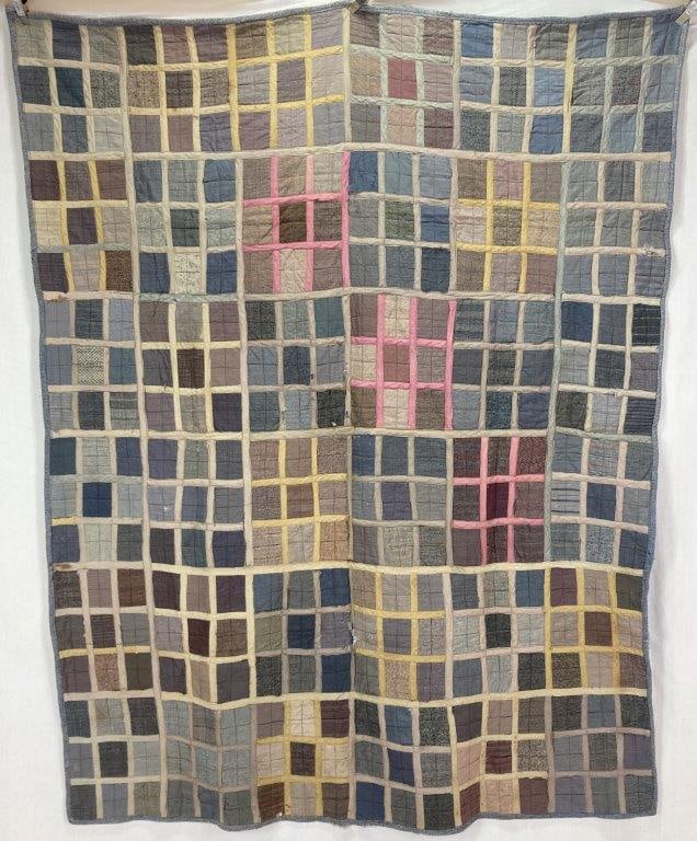 African American Patchwork Quilt: This African American patchwork quilt features a structured grid layout creatively constructed from mixed utility fabric scraps. The pieced design is framed by sashing that highlights distinct pink