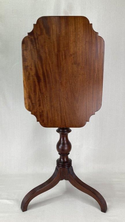 19th Century Cherry Tilt Top Table: A handsome 19th century cherry tilt top table featuring a rectangular top with serpentine outline and molded edge, raised on a finely turned vase-shaped post terminating in a tripod base with reeded