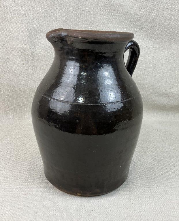 Glazed Stoneware Pitcher: Handsome glazed stoneware pitcher showcases a rich, deep brown glaze that emphasizes its classic utilitarian silhouette. The vessel features a striking incised decorative band around the upper body,