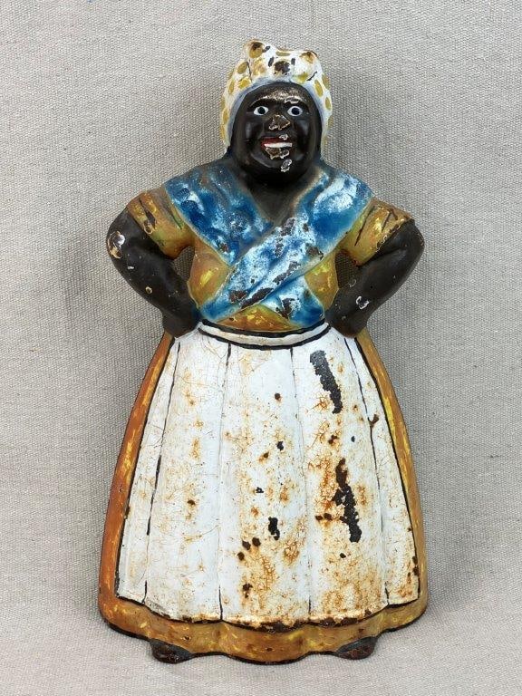 Cast Iron Mammy Black Americana Doorstop: A cast iron Black Americana doorstop in the form of a Mammy figure, dressed in a traditional outfit with vibrant original paint in shades of blue, yellow, orange, and white. The figure displays a wond