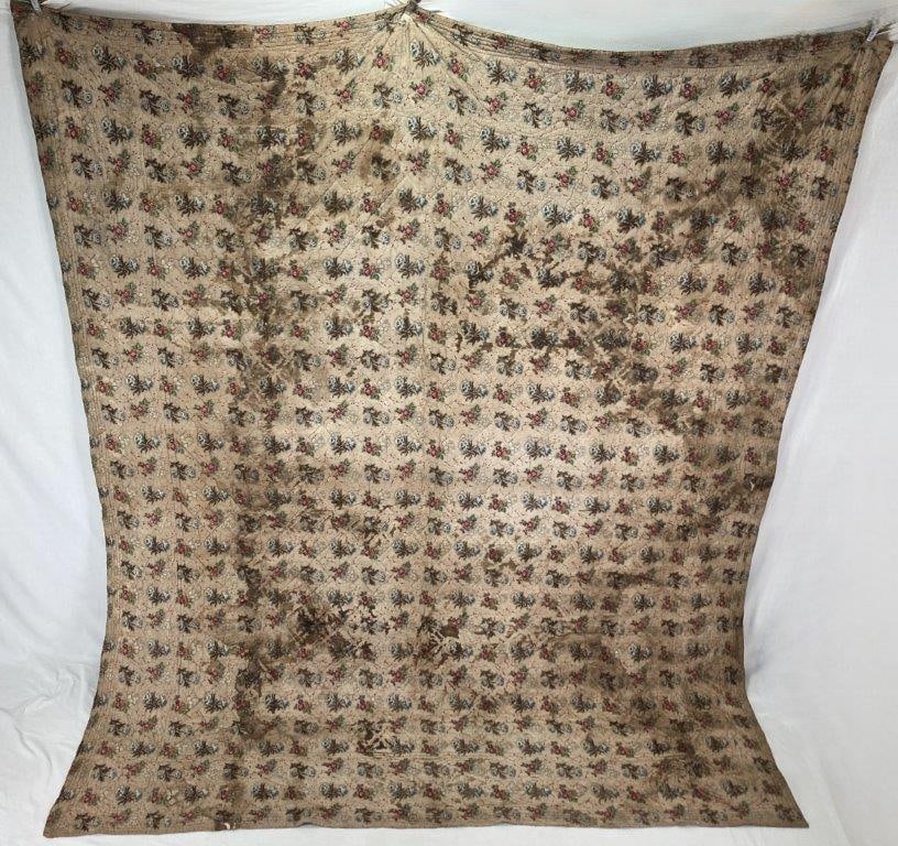 19th Century Chintz Quilt: This 19th-century chintz quilt features a repeating floral motif pattern on a tan ground. Showcasing a versatile double-sided design, the textile reverses to a dark ground with a red and white