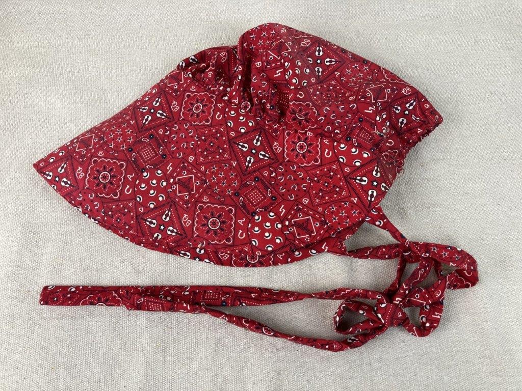 Early 20th Century Red Bonnet: Charming early 20th-century bonnet features a vibrant red form adorned with delicate decorative patterning, beautifully capturing a nostalgic and quaint country aesthetic. Measuring approximately 10