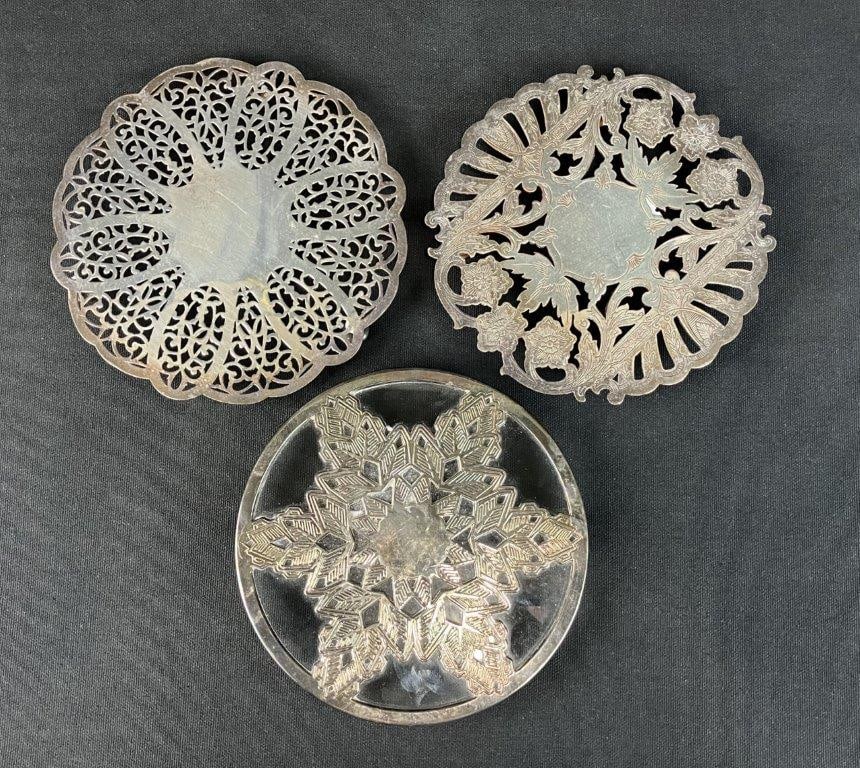 Three Silver Plate Trivets: Three silver plated trivets showcases the timeless sophistication and practical utility of vintage tabletop dining accessories. Highlighting the trio is a beautifully crafted piece by the renowned