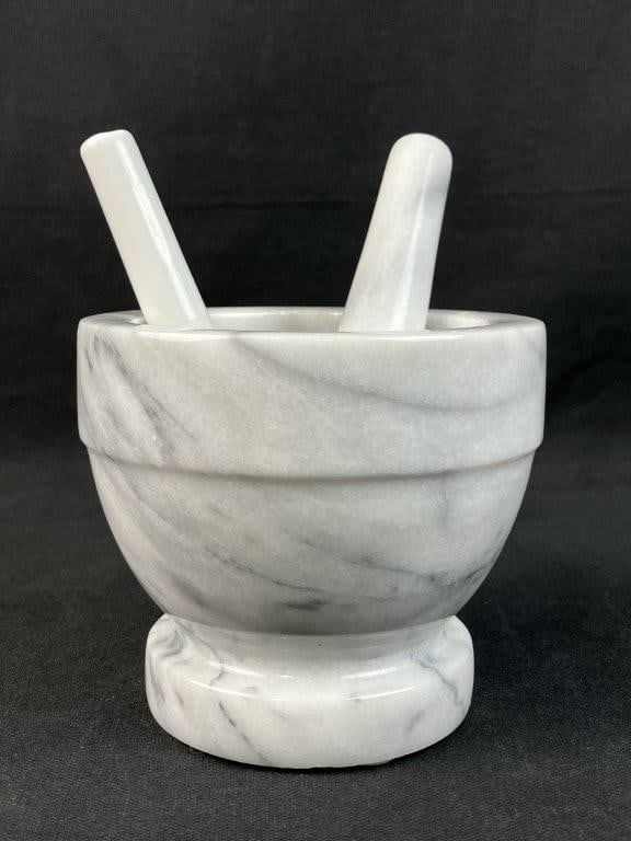 Marble Mortar and Pestle: This traditional mortar and pestle set is crafted from a soft, cool white marble characterized by its distinctive, rich grey veining. The piece features a classic, heavy form that balances functional