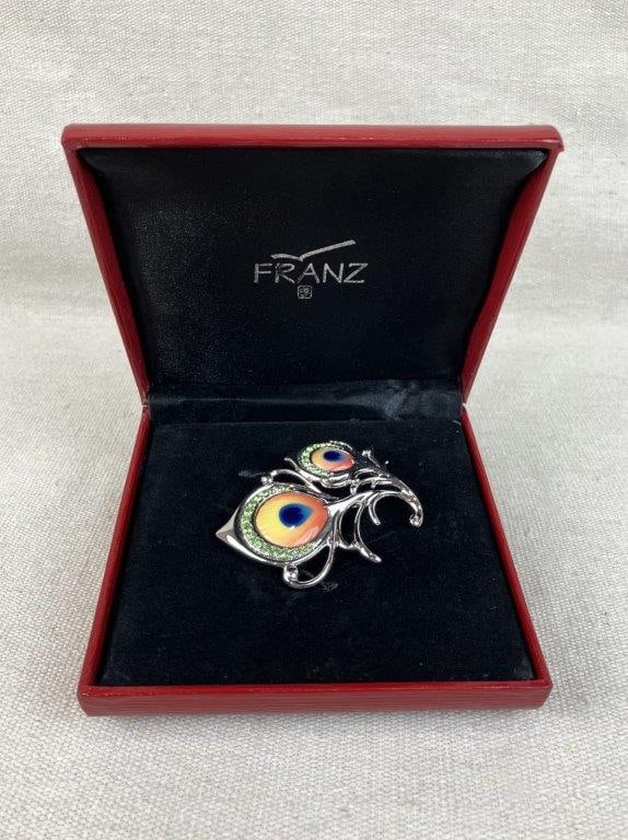 Franz Designer Porcelain Peacock Brooch: Substantial, artfully designed brooch features hand-painted inset porcelain accented with vibrant green rhinestones. It is set in a silvertone, feathered-motif metalwork. The brooch measures