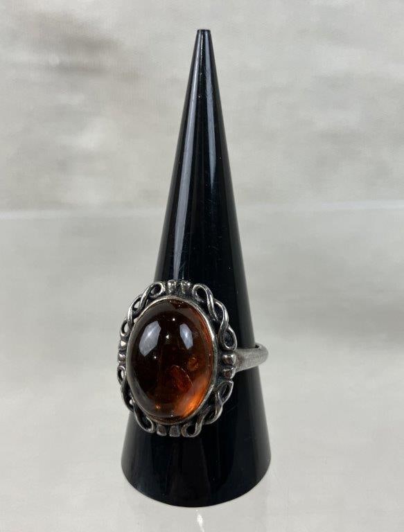 Artisan Sterling Silver and Amber Ring: Striking piece features a distinctive artisan aesthetic, centered around a polished, warm-hued amber cabochon. The stone is framed by a delicate twisted metal border, set atop a sleek, streamlined