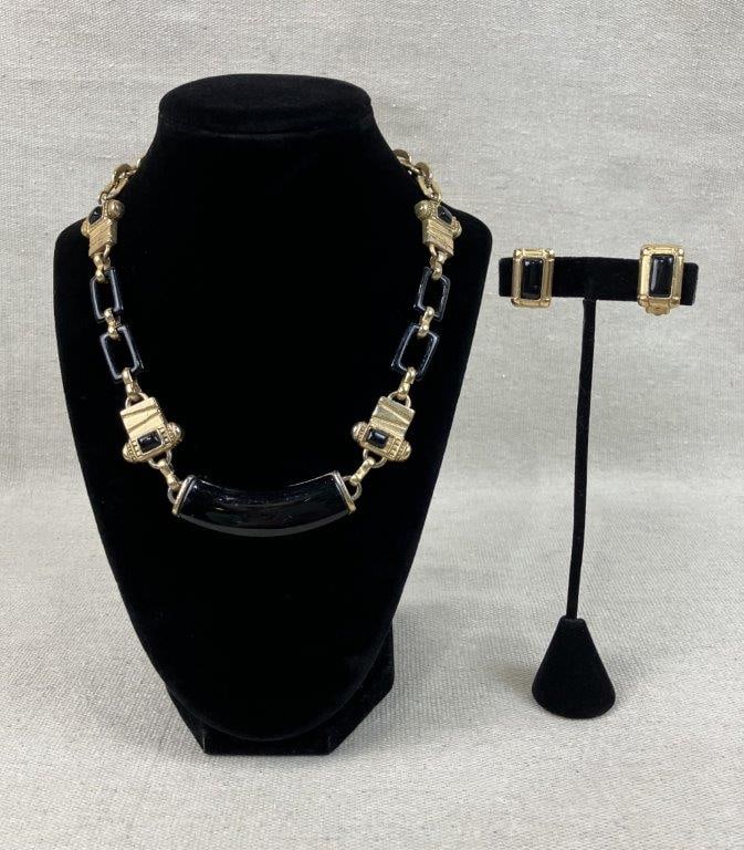 Gold-tone Art Deco Revival Necklace and Earrings: This demi-parure features an elongated, curved central black enamel bar on the necklace, anchored by ornate spacer beads and black geometric links, finished with a toggle clasp. The set includes a