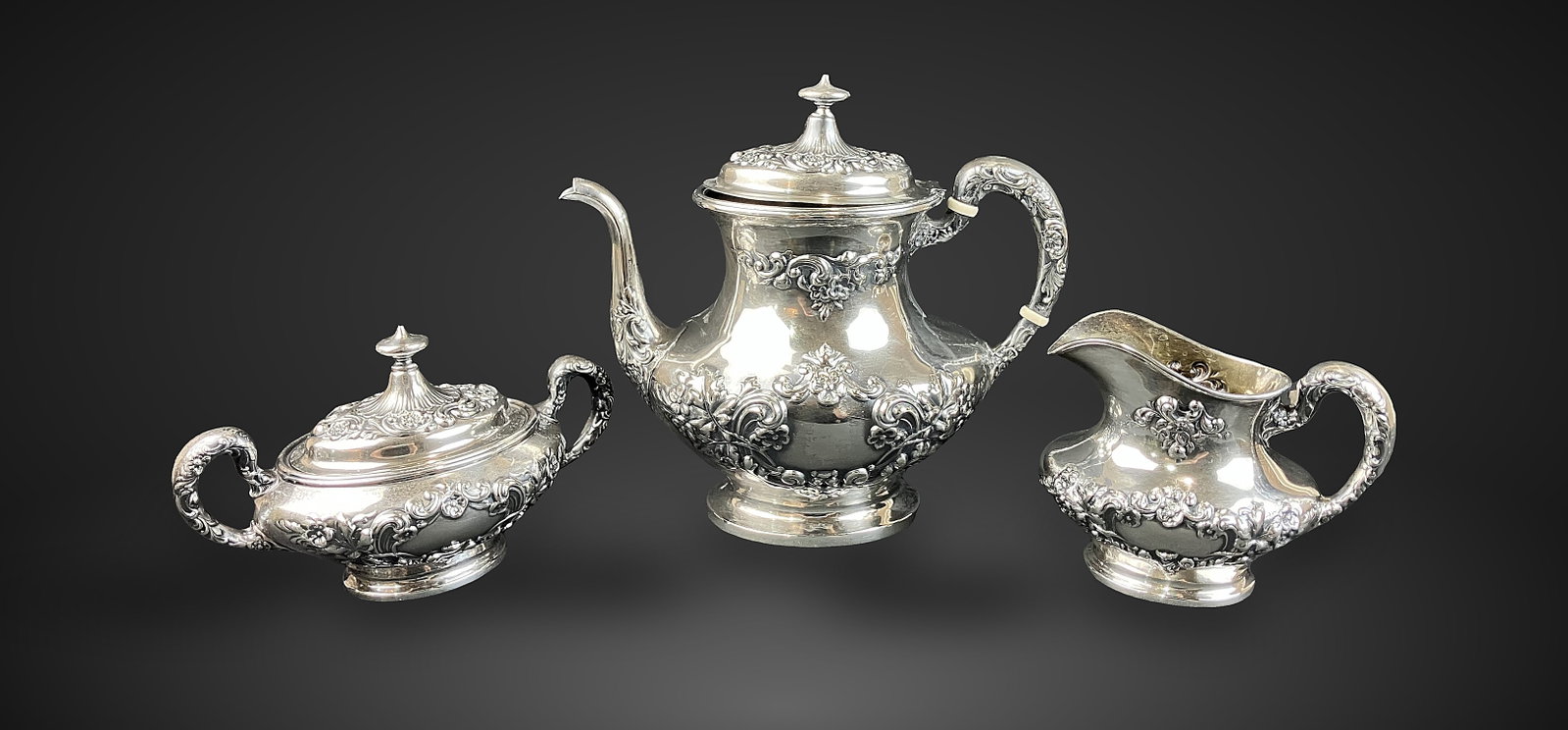 Gorham Sterling Silver Tea Set: Elegant set includes a teapot, creamer, and a covered sugar bowl, all executed in the intricate, floral-inspired Buttercup repousse pattern. Dramatic curving form with decorated surfaces