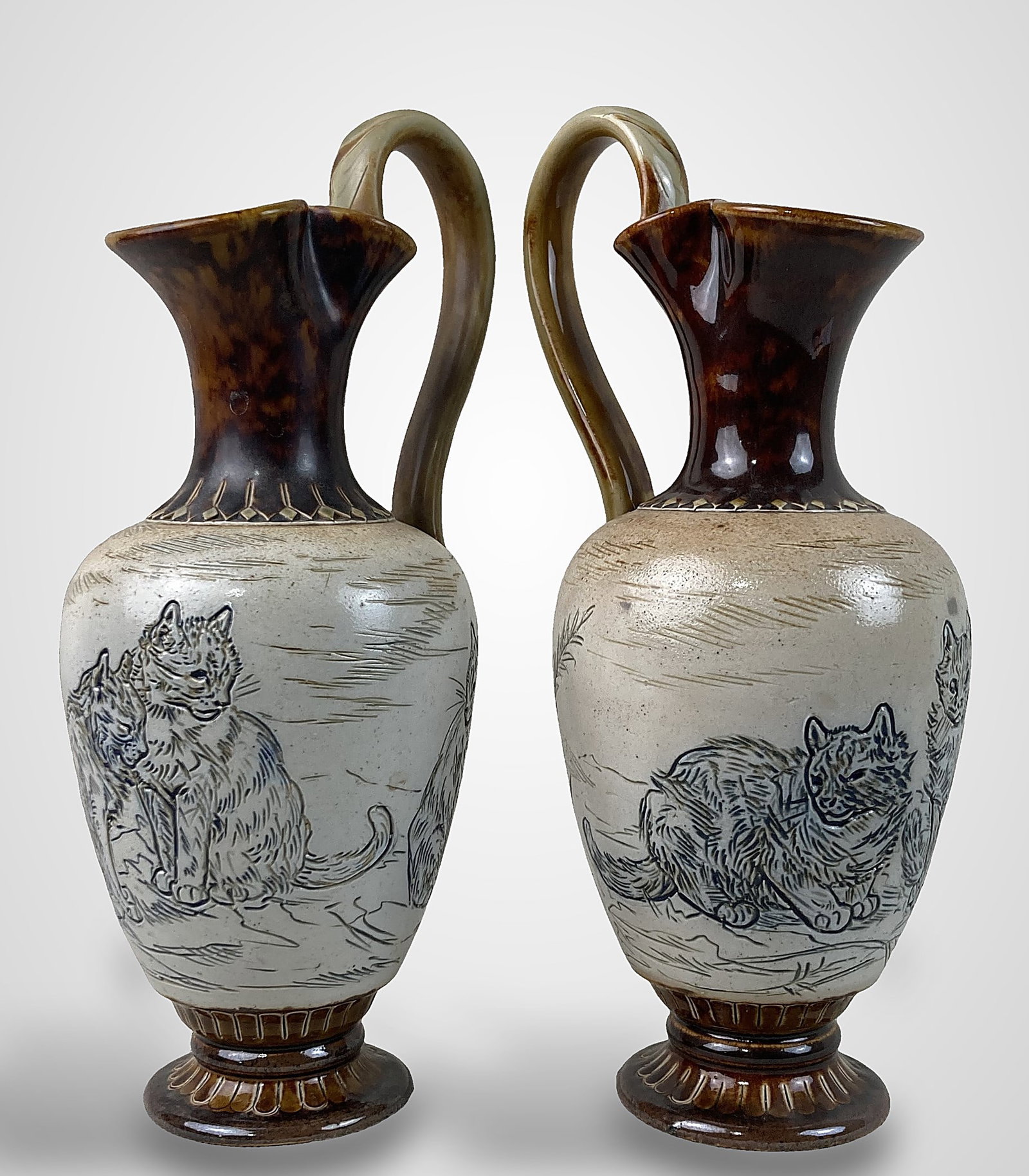 Pair of Hannah Barlow Doulton Lambeth Cat Pitchers: Pair of pitchers is signed with the characteristic Hannah B. Barlow double B mark featuring a central H. Each piece displays a landscape scene populated with cats, executed in the expert sgraffito