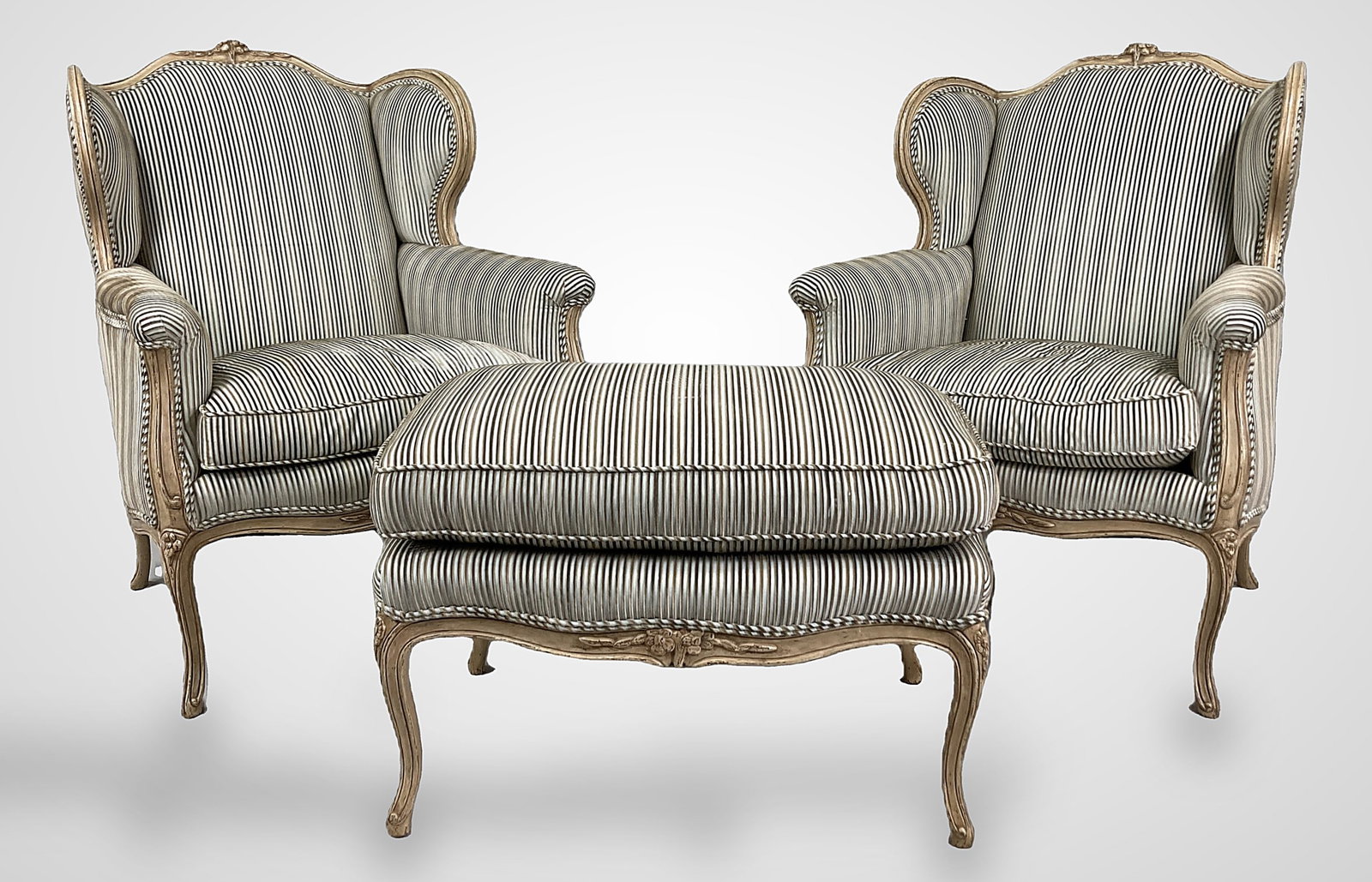 Pair Of Louis XV Style Bergere Wingback Chairs And Ottoman: An elegant pair of oversized French Louis XV style bergere wingback chairs with matching ottoman, each chair featuring a gracefully shaped crest back surmounted by a carved floral bouquet, serpentine 