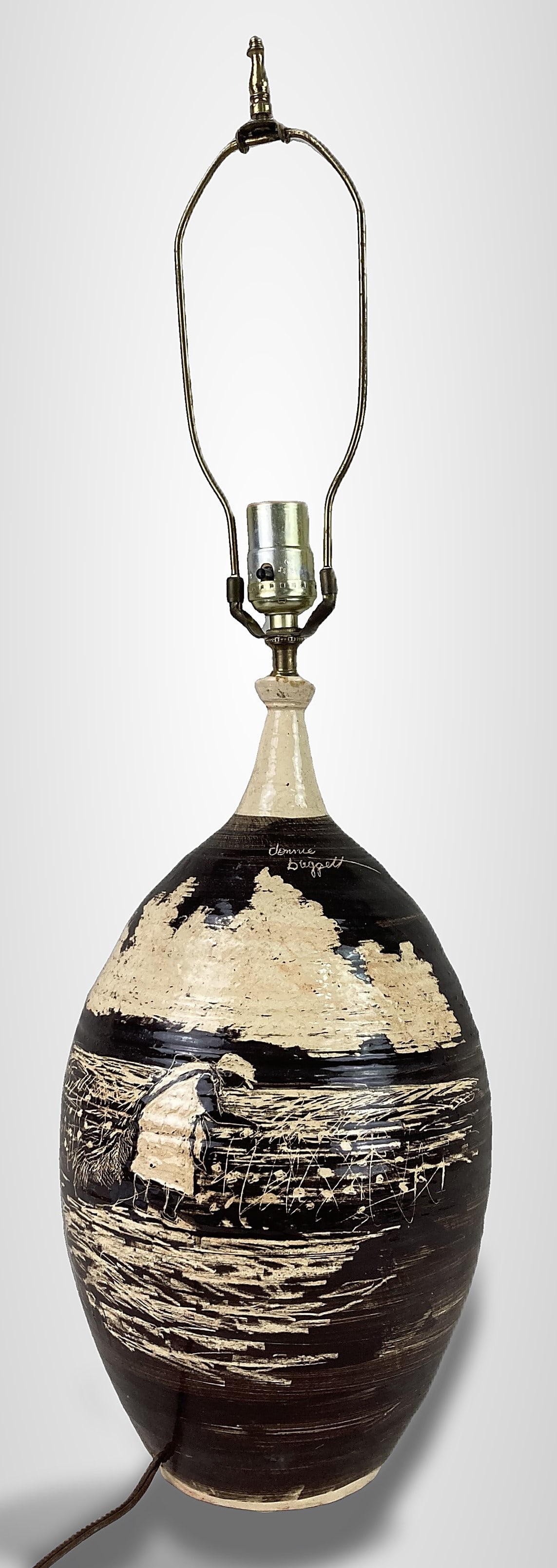 Donnie Baggett Pottery Table Lamp: This hand-crafted ceramic lamp by Mississippi potter Donnie Baggett features a detailed sgraffito design depicting a rural scene with a cotton picker in the foreground set against clouds. The piece