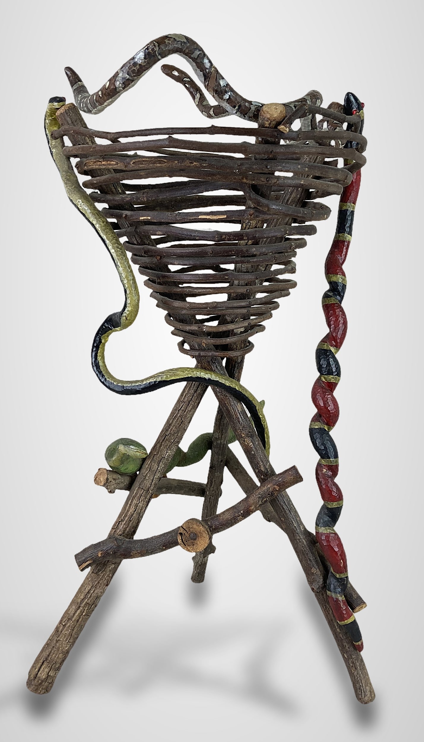 North Carolina Carved Folk Art Snake Basket: This piece features a wicker woven funnel-style basket supported by three intersecting splayed natural wood logs connected with simple cross bracing. It is adorned with four carved and hand-painted