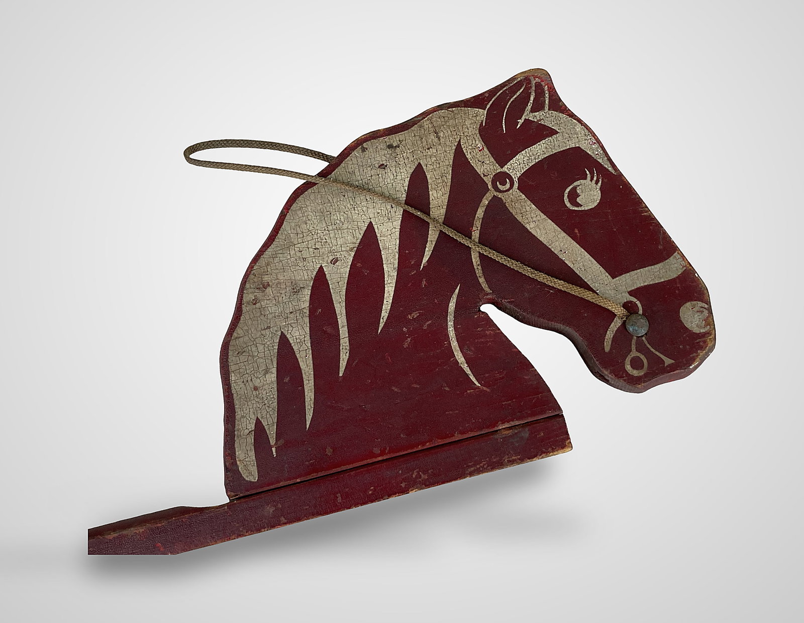 Antique Wood Hobby Horse: This piece features a cut-out profile horse head finished in a dark red paint with off-white accents on the face and hair, and is fitted with a simple rope strap. The head is mounted on a long,