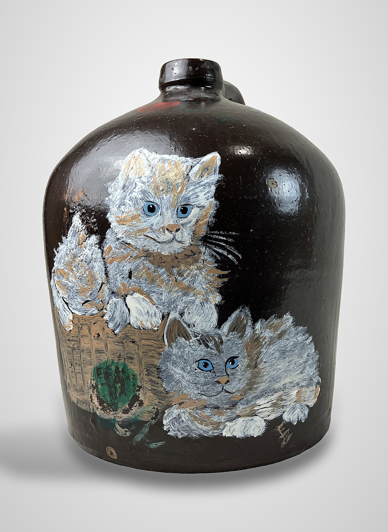 Folk Art Cat Painted Stoneware Merrill Company Jug: Albany-slip stoneware jug features a defined lip, an applied handle, and a rounded shoulder. It is decorated with a hand-painted motif of three striped white cats with a basket, complemented by a