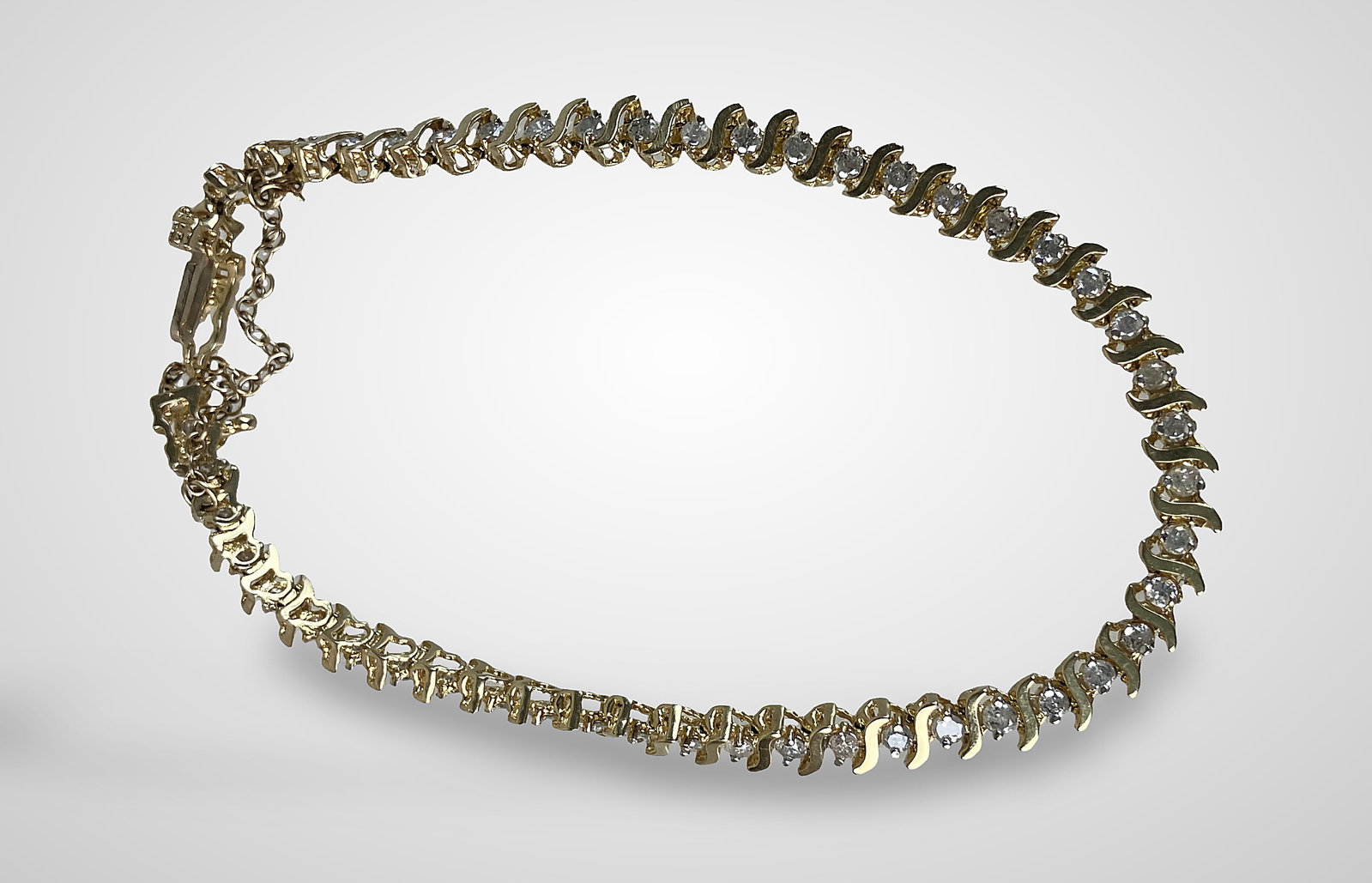 10KT Gold Diamond Tennis Bracelet: Elegant bracelet features 50 round or brilliant-cut diamonds totaling 1 CT, set in 10KT yellow gold. The design showcases an articulated chain with swirling forms interspersed between the stones. It