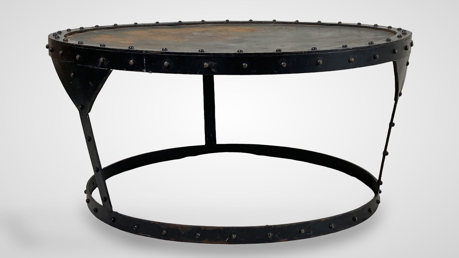 Iron Industrial Style Coffee Table: An iron industrial style coffee table, the round dark-finish metal top adorned with riveted detailing around the edge and supported by a metal frame, the whole presenting a distinct, rustic