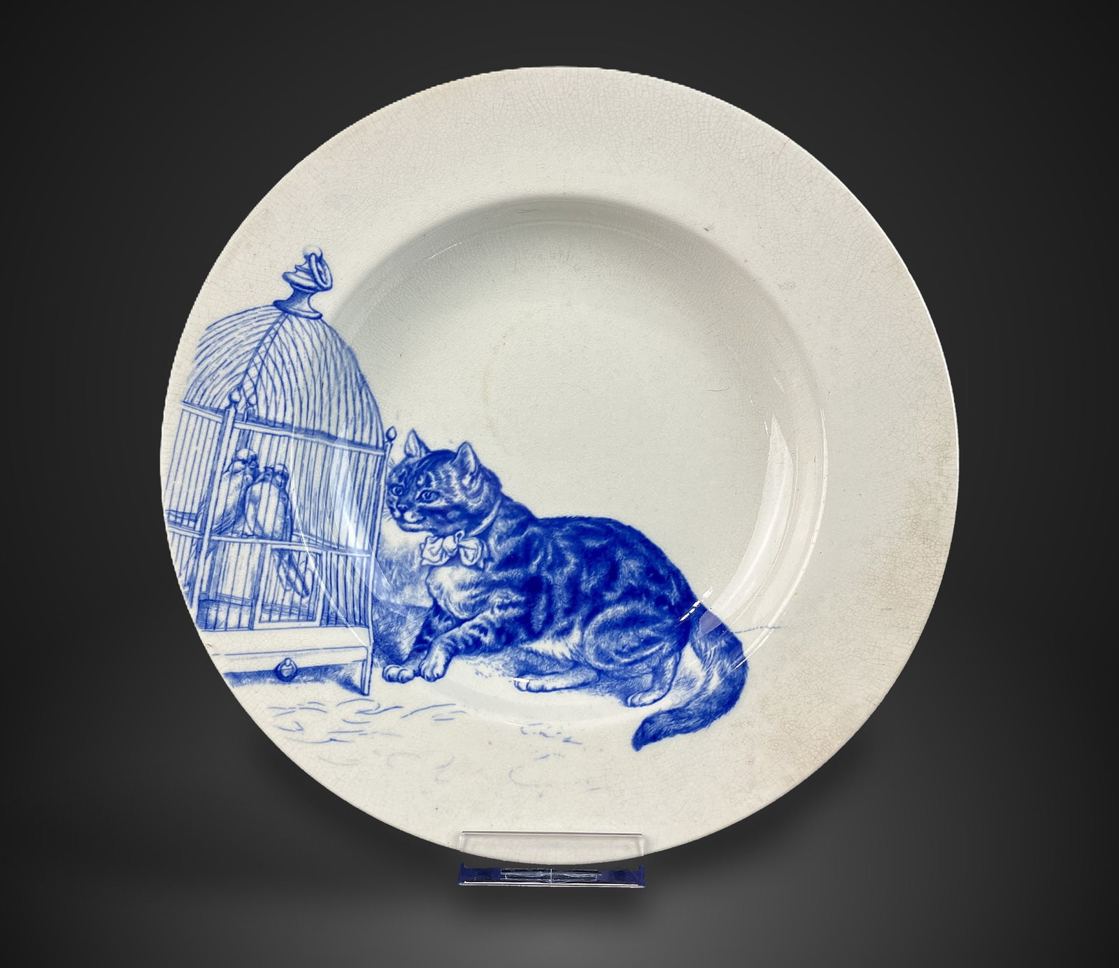 Minton Transferware Cat Soup Plate: Late 19th Century blue and white transferware piece features a Minton mark on the base. The design depicts a tabby cat seated before a bird cage. It measures approximately 1 1/4 in. H x 10 1/4 in. in