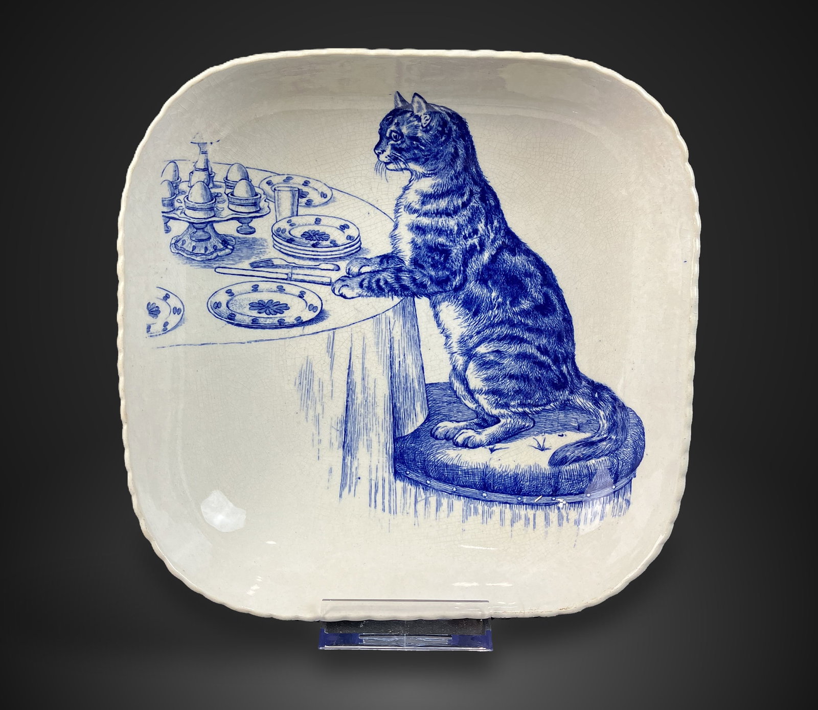 Minton Transferware Cat Dish: Early 20th-century blue and white transferware piece features a Minton laurel wreath mark on the base. The design depicts a tabby cat seated at a dining table, framed by a delicate basket-weave