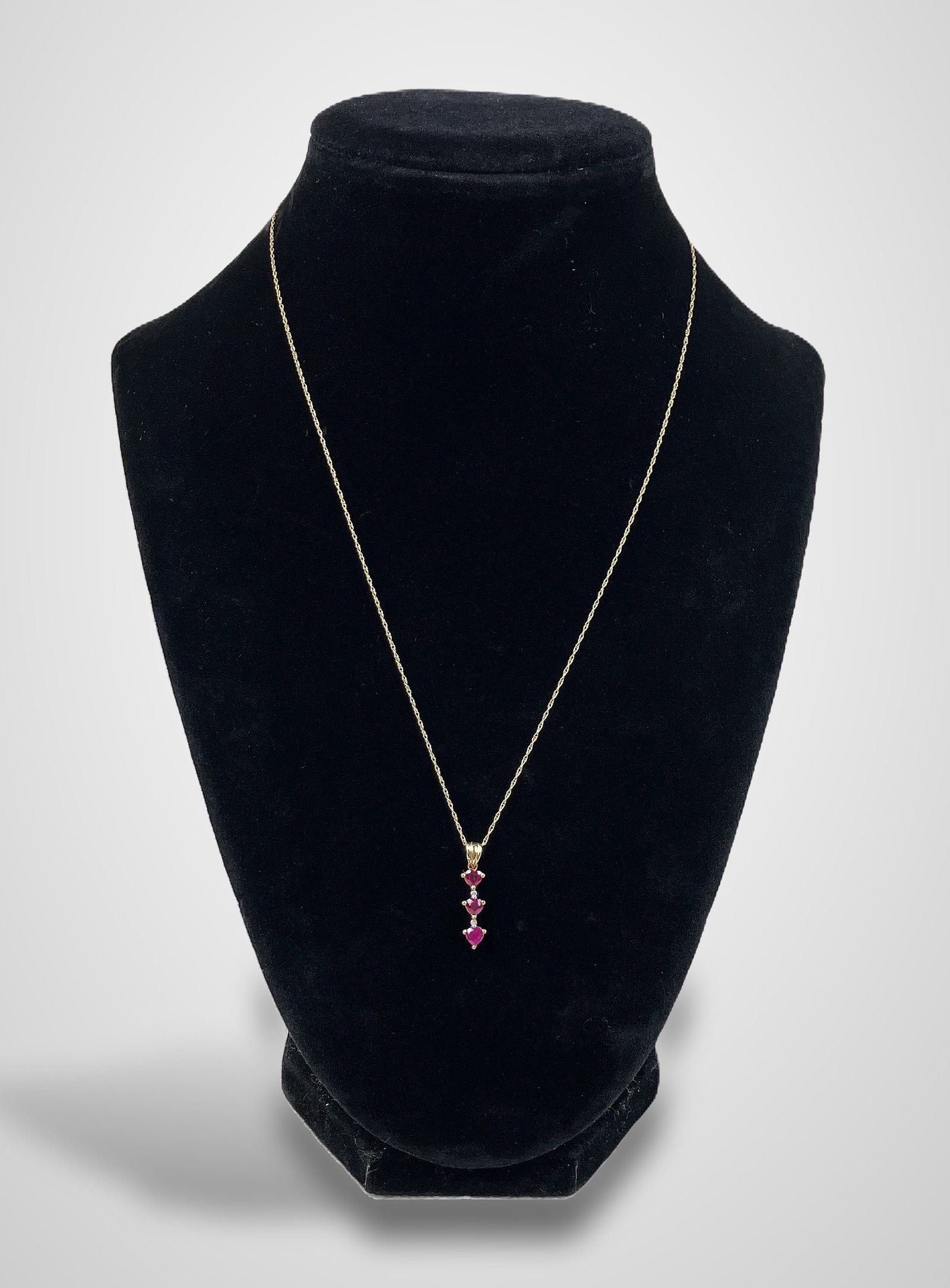 10 KT Gold, Diamond, and Ruby Necklace: Warm 10KT gold piece features a pendant with three cut rubies interspersed between three smaller diamonds. The necklace measures 17 in. in length, and the pendant measures approximately 1 in. in