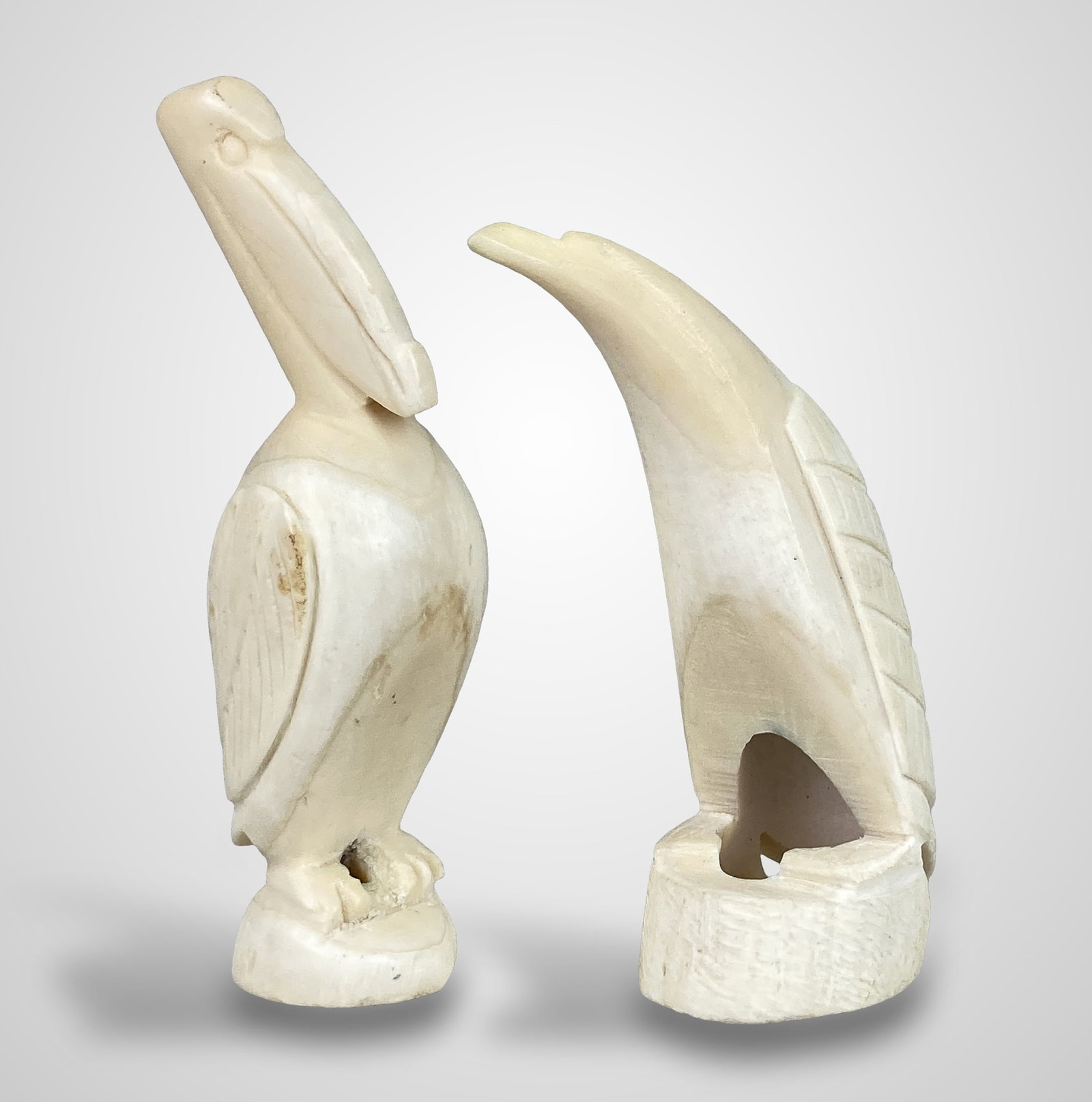 Scrimshaw Carved Bird Figures: Two carved bone figures including a pelican with an elongated beak and a penguin depicted with an outstretched neck. Both pieces feature detailed score lines accentuating the wings and bodies.