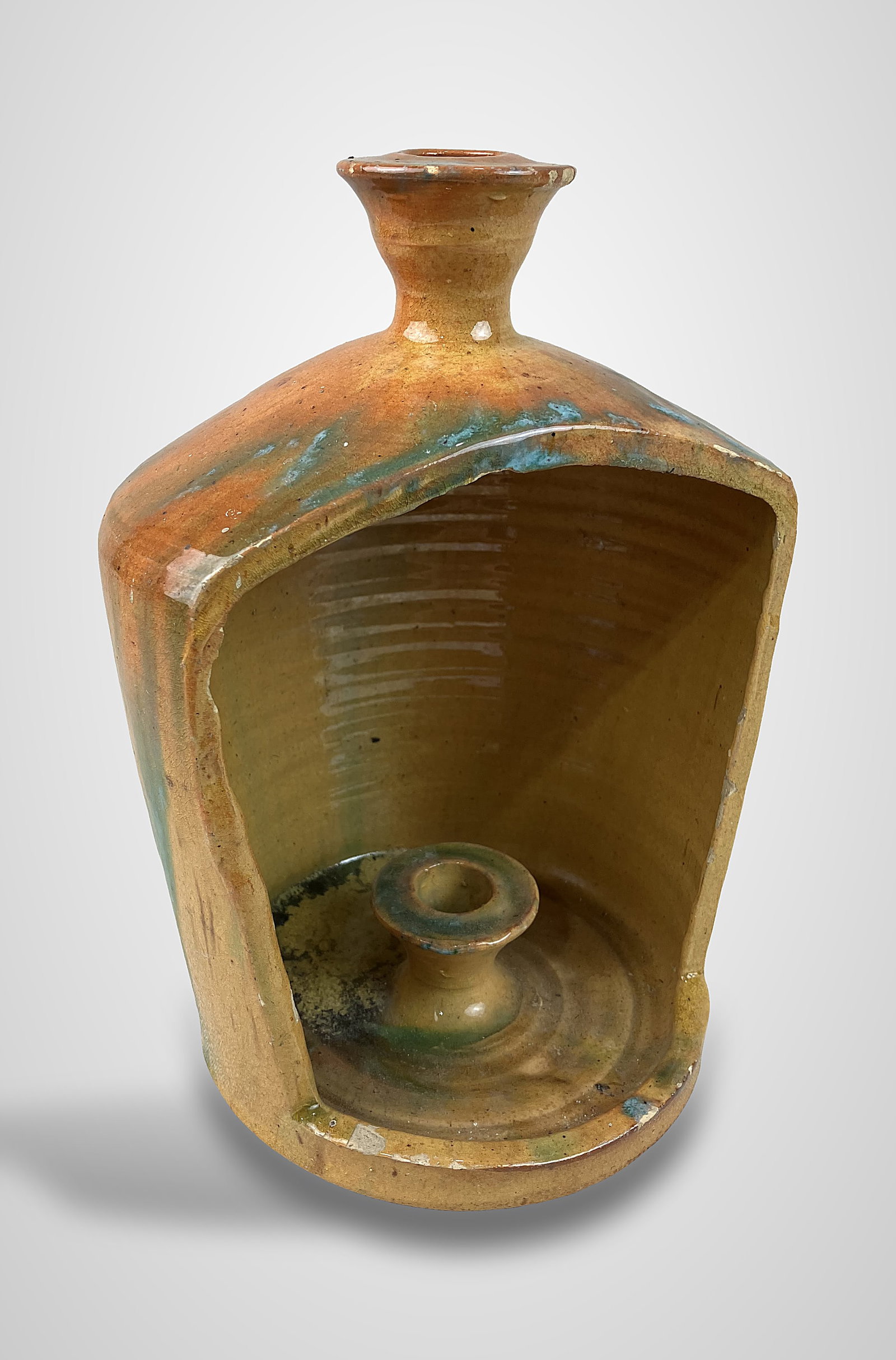 North Carolina Studio Pottery Jug Lantern: Piece features a jug-shaped form with an open front, designed to display a candle within its dedicated stick component. It is finished with a striking blue-green runny drip glaze over a warm, sienna-o