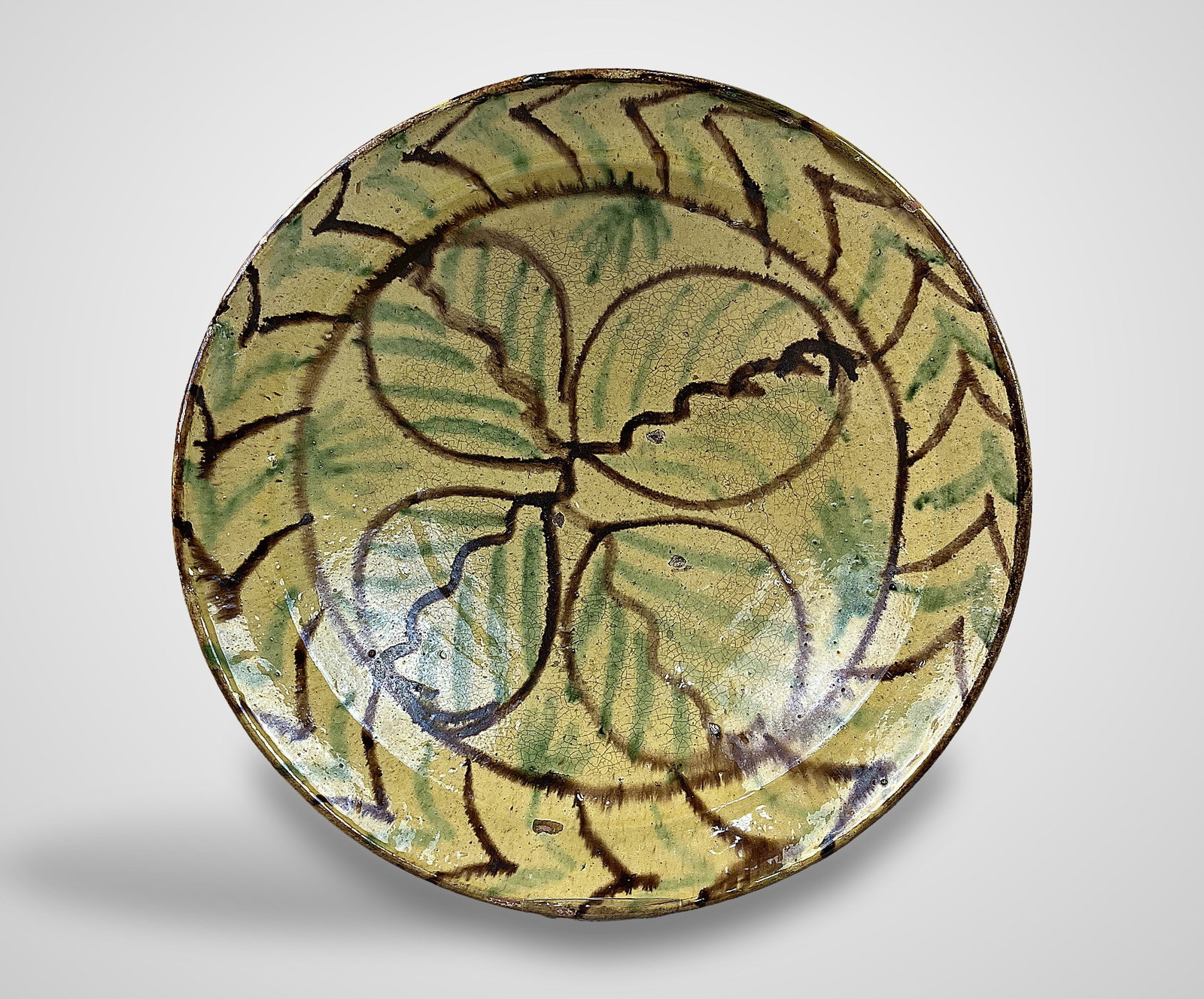 Early American Slip Decorated Bowl: Substantial bowl features a classic leaf motif complemented by a geometric border, rendered in green and brown slip against a soft yellow ground. It measures approximately 3 3/8 in. H x 11 7/8 in. in
