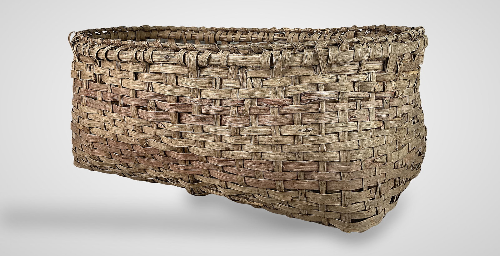 Large Country Storage Basket: This nicely woven split oak storage basket features a two-tone coloration, a wrapped rim, and open handles on the sides. It is constructed with an oval rim and a rectangular base and displays a worn, 