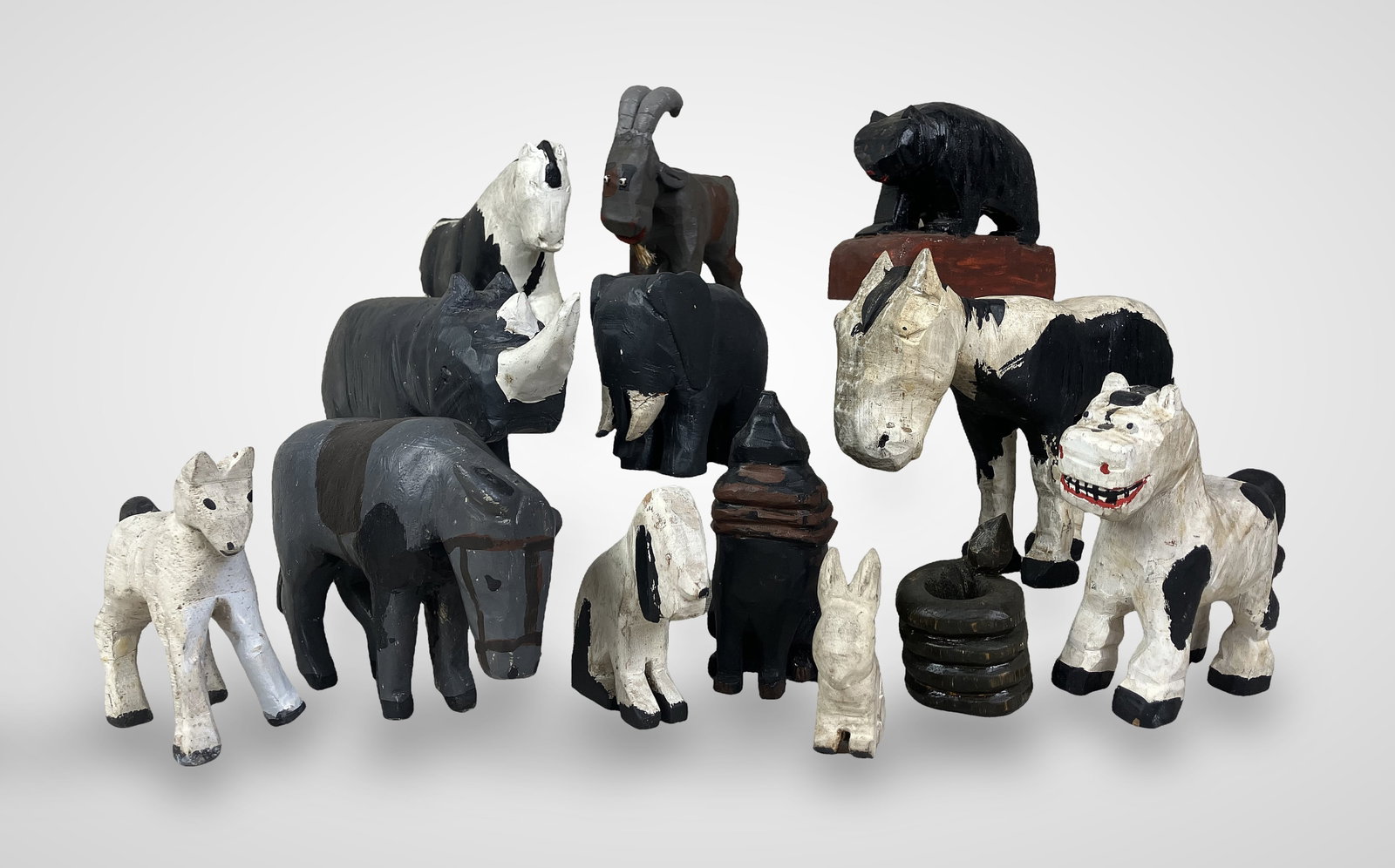 Folk Art Carved Animal Figures: Thirteen primitively carved animal figures, including a donkey with a white and black painted body, a rhino with a dark grey body and white horns, a carved coiled rattlesnake, an elephant, and a