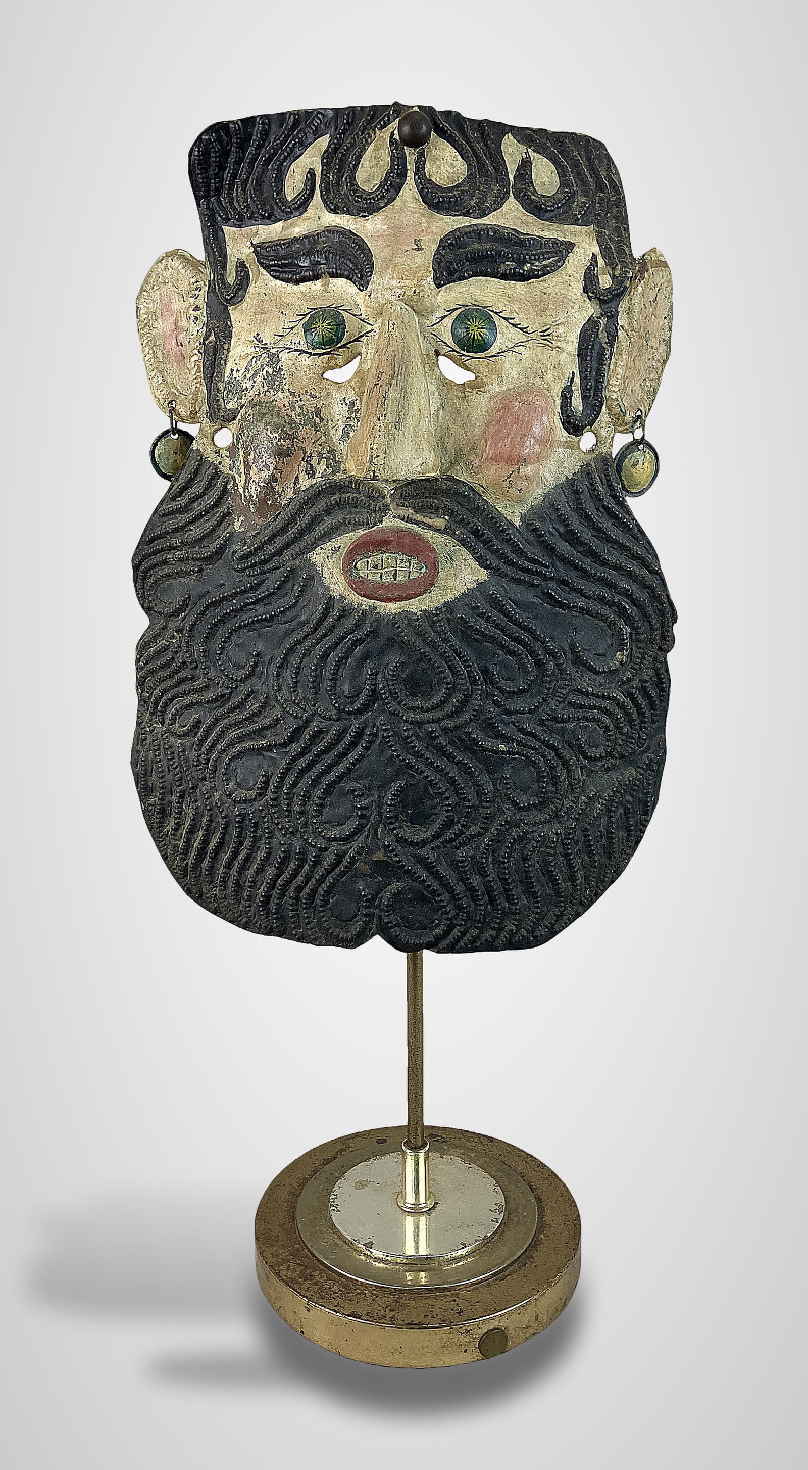 Mexican Guerrero Barbones Man Mask: Folk art barbones (bearded man) mask from Guerrero, Mexico, is crafted from polychromed, hammered metal and mounted on a brass base. Measuring approximately 24 1/2 in. H x 10 in. W x 7 5/8 in. D, the
